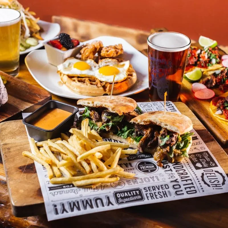 Table of sandwiches, fries, chicken and waffles, and beer.