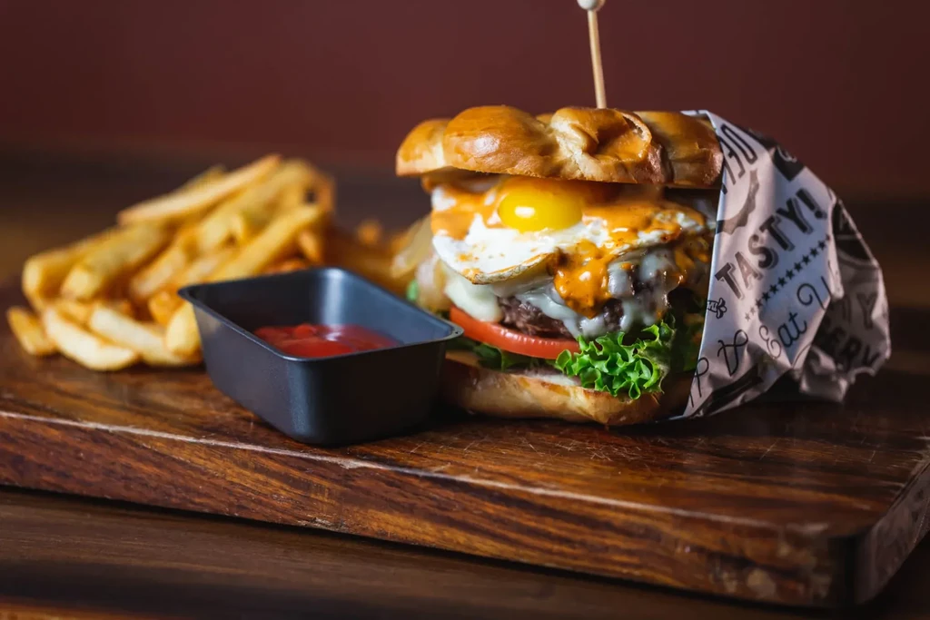 Burger with a fried egg, fries, and ketchup on a wooden board.