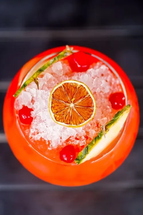 Overhead shot of an orange cocktail with ice, dried orange, cherries, and pineapple.