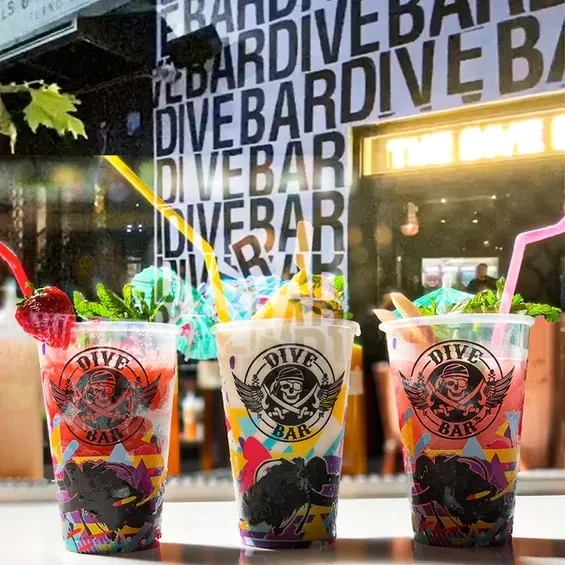 Three colorful drinks with straws on a bar with a "DIVE BAR" sign.