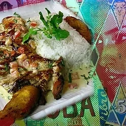 Grilled whole fish with rice, plantains, and sauce on a colorful table.