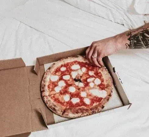 Tattooed hand reaching for a pizza slice in an open box.