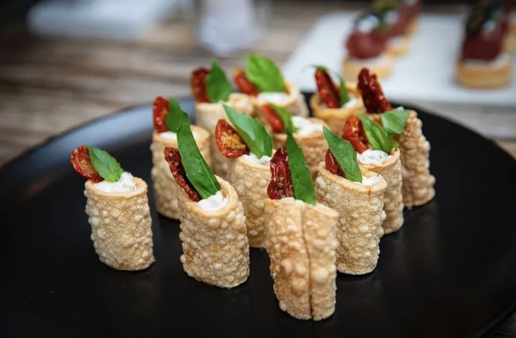 Appetizers with sun-dried tomatoes, basil, and cheese served on a black plate.