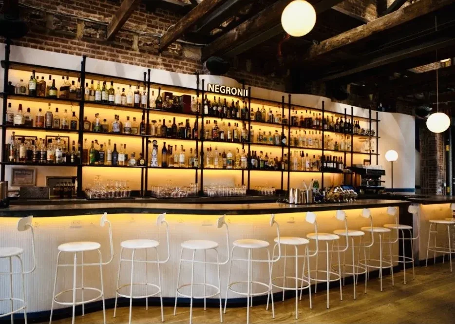 A long, well-stocked bar with white stools and warm lighting.