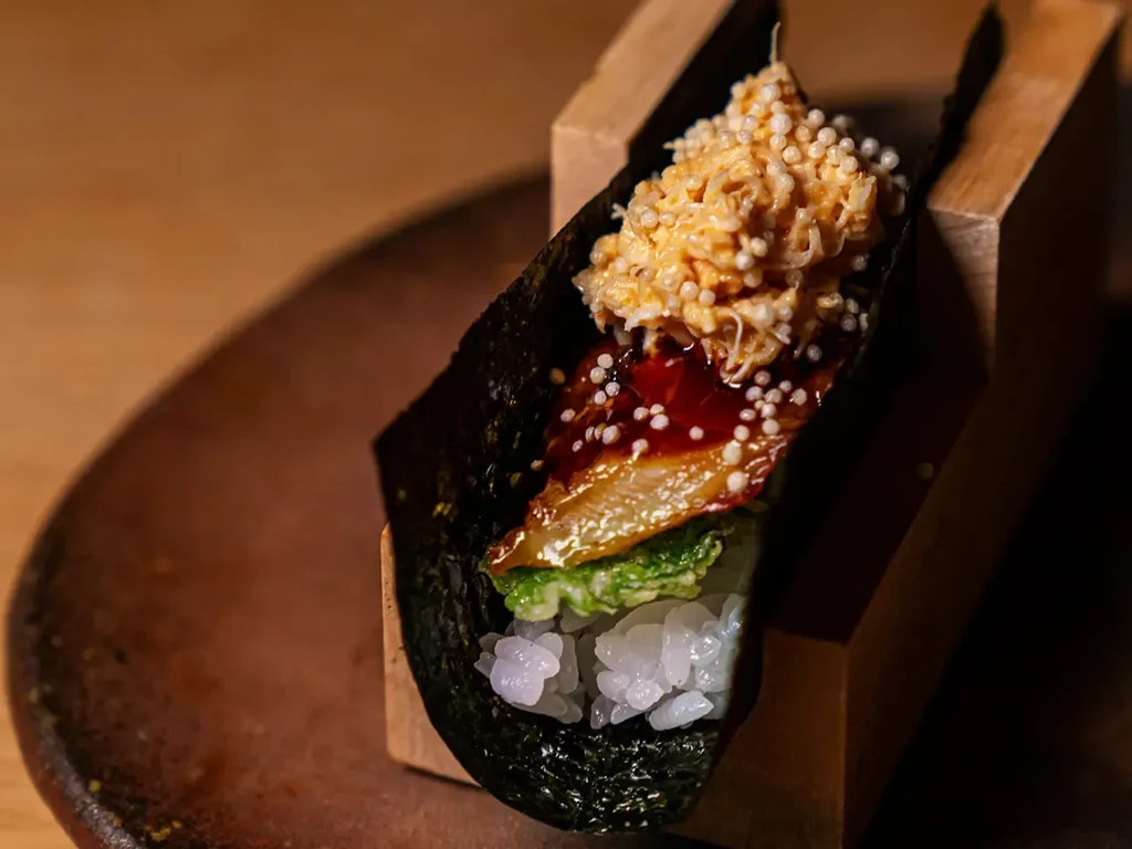 A handroll with eel, crab, rice, and green vegetables.