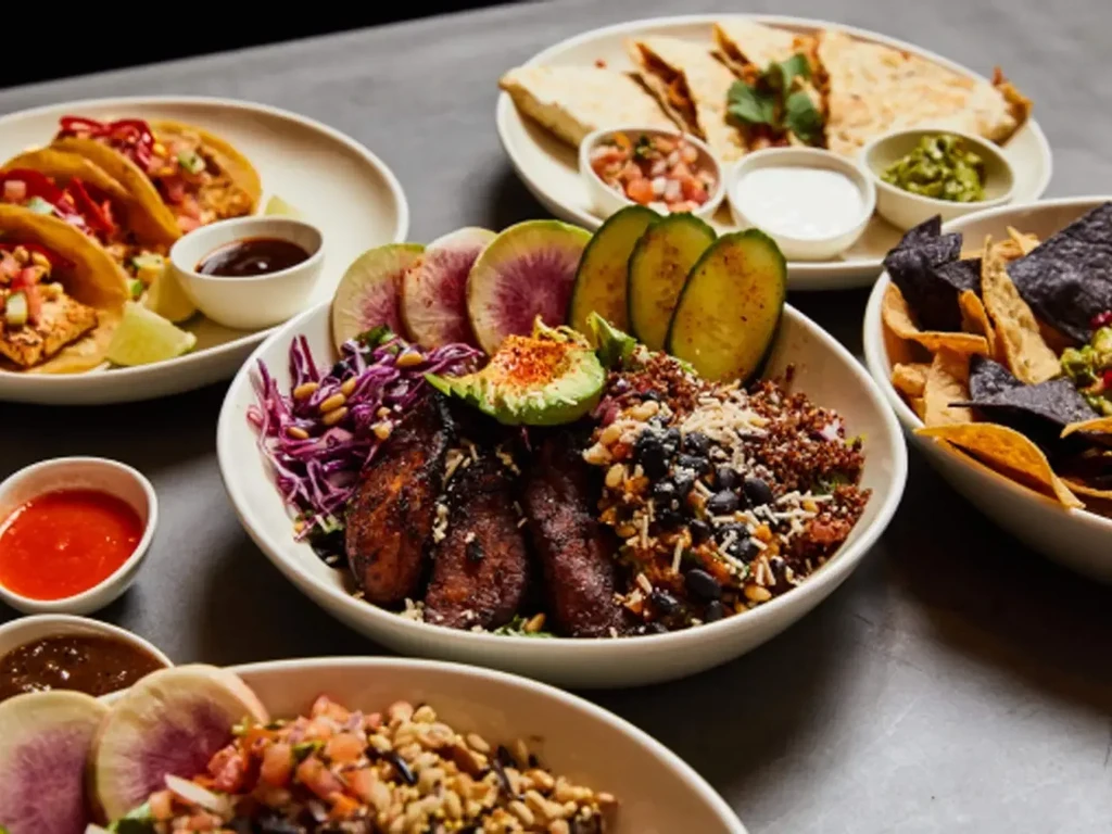 Various dishes including tacos, quesadillas, and grain bowls on a table.
