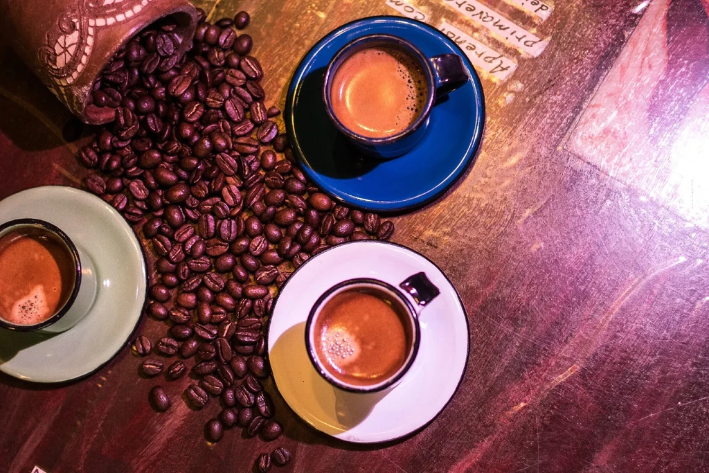 Three espresso cups with roasted coffee beans spilling from a container.