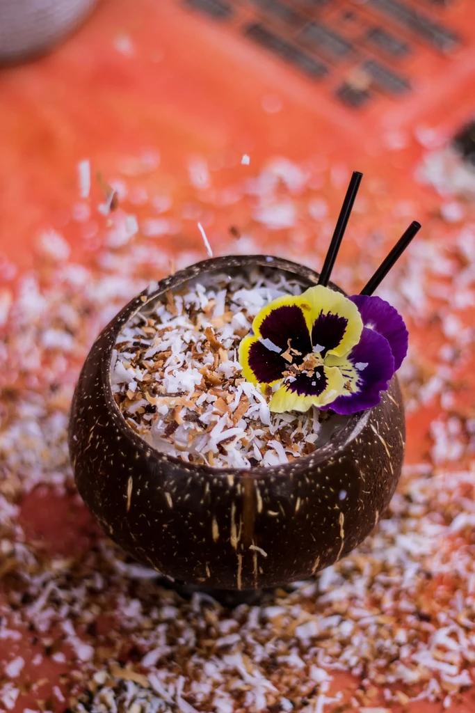 A coconut shell filled with white flakes, decorated with two pansy flowers.