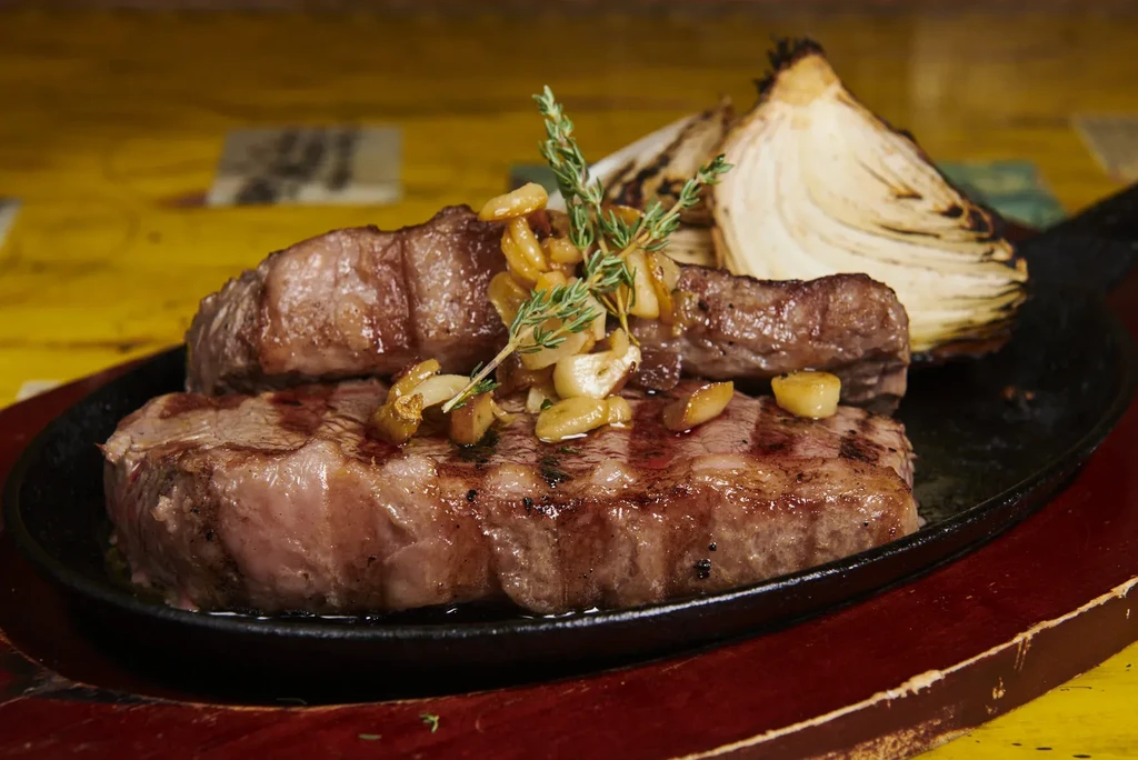 Two steaks topped with garlic and thyme, with charred onion.