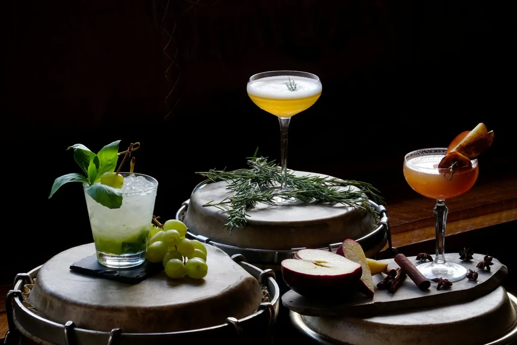 Three cocktails with fruit and herbs on drum heads.