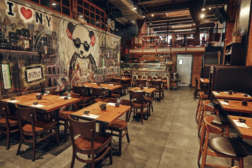 Empty Asian fusion restaurant interior with a large panda mural and wooden tables.