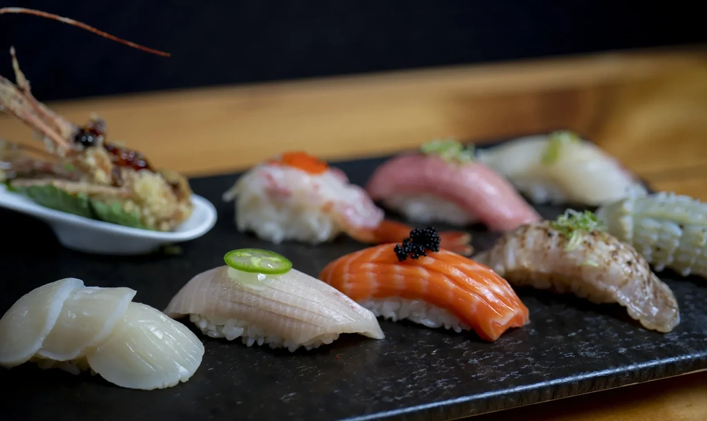 Variety of sushi nigiri and tempura shrimp on a black plate.