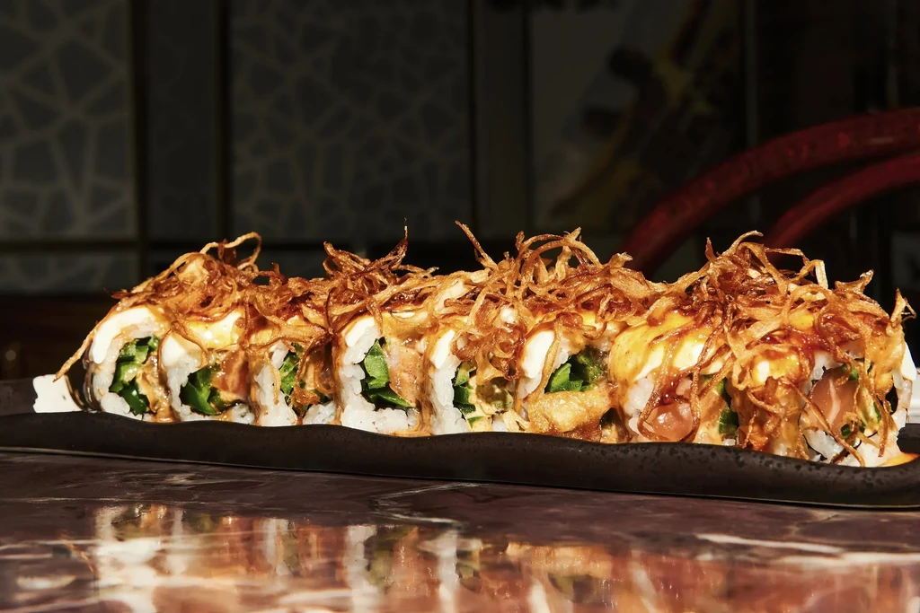 Sushi rolls topped with crispy fried onions on a black plate.