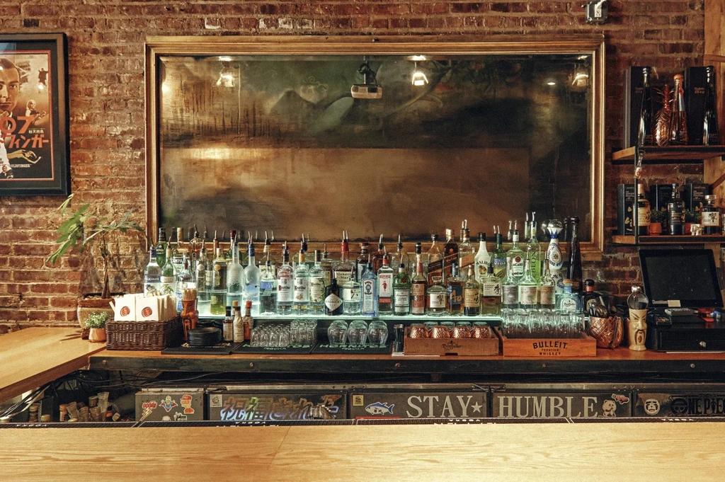 A well-stocked bar with a mirror, brick wall, and "STAY HUMBLE" sign.