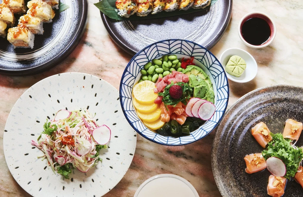 An overhead shot of a sushi and poke bowl meal on a marble table.