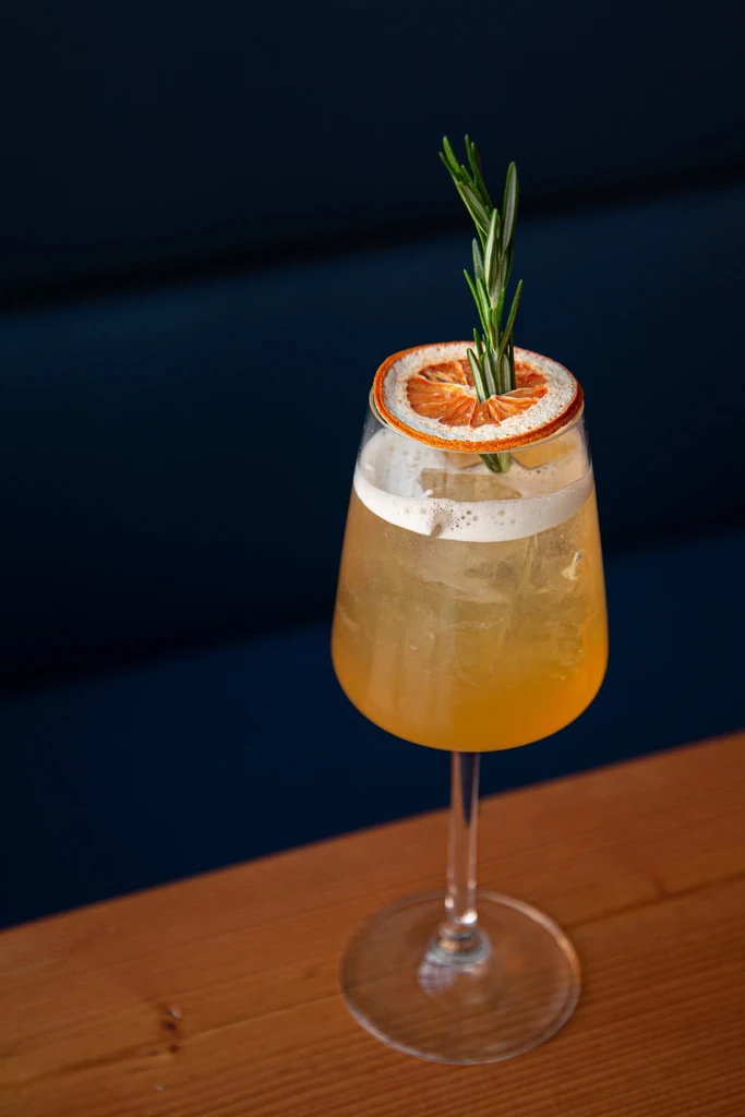Cocktail in stemmed glass, garnished with dried orange and rosemary.