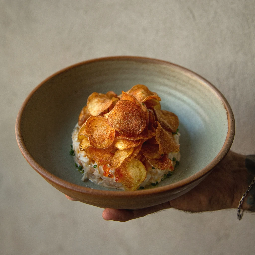 A hand holds a ceramic bowl of rice topped with golden potato chips.