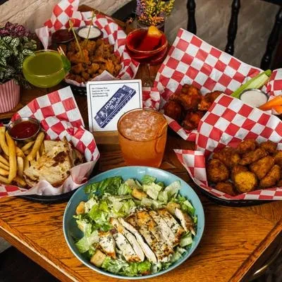 An overhead shot of four baskets of food and two drinks on a wooden table.