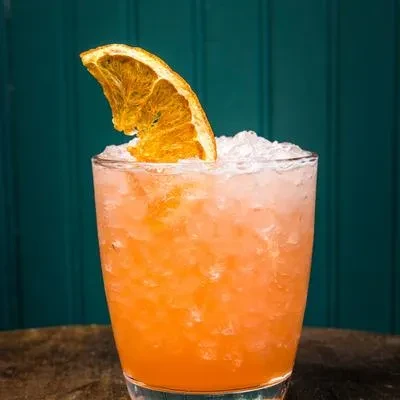 A vibrant orange cocktail with crushed ice and a dried orange slice.