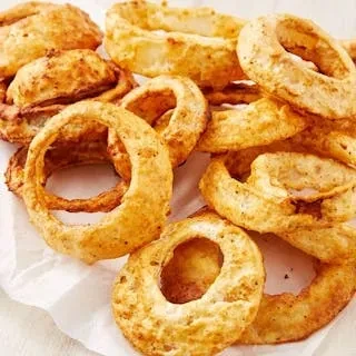 A pile of golden-brown onion rings and breaded items on a white surface.