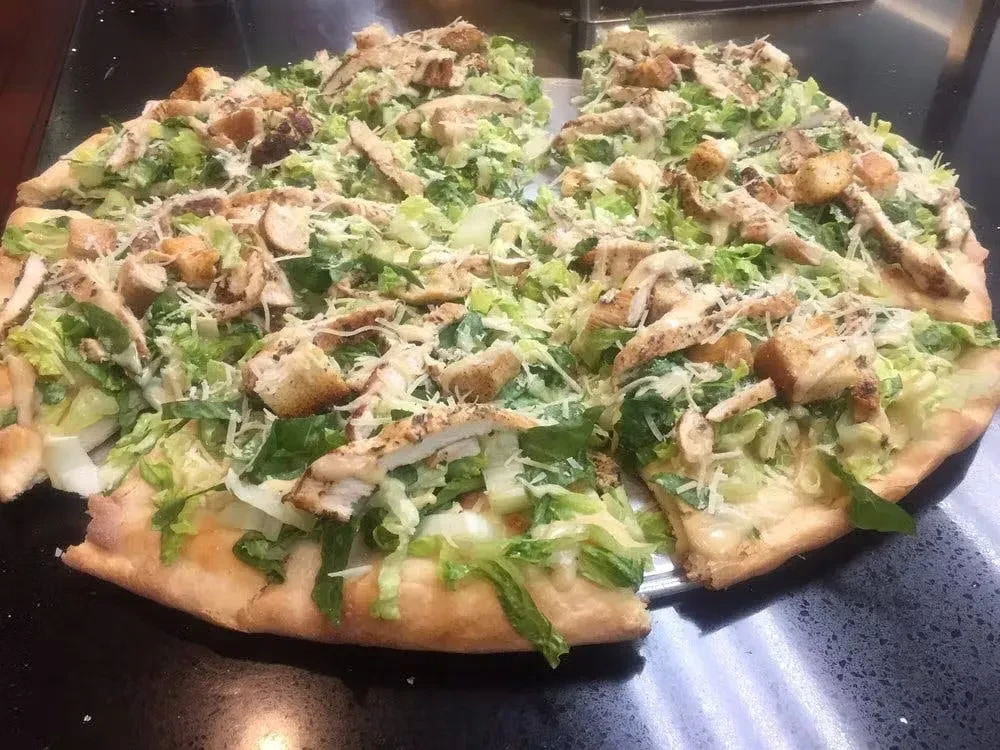 A Caesar salad pizza with chicken, lettuce, croutons, and cheese.