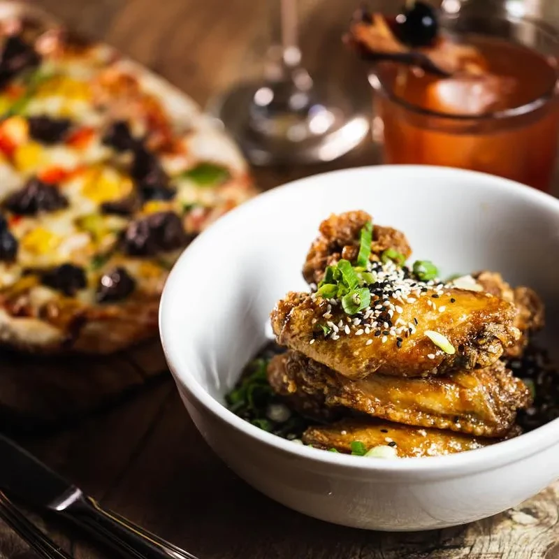 A bowl of sesame chicken wings with pizza and a drink.