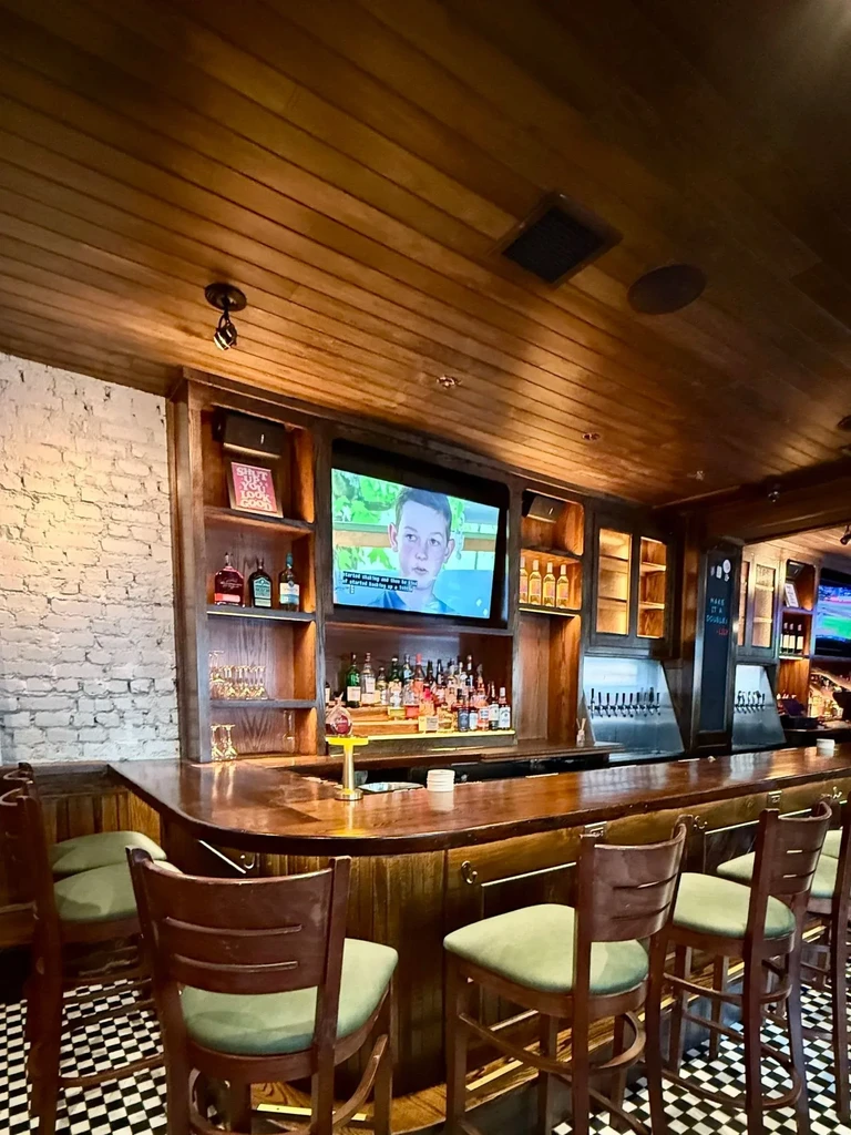 A wooden bar with green stools and a TV playing a show.