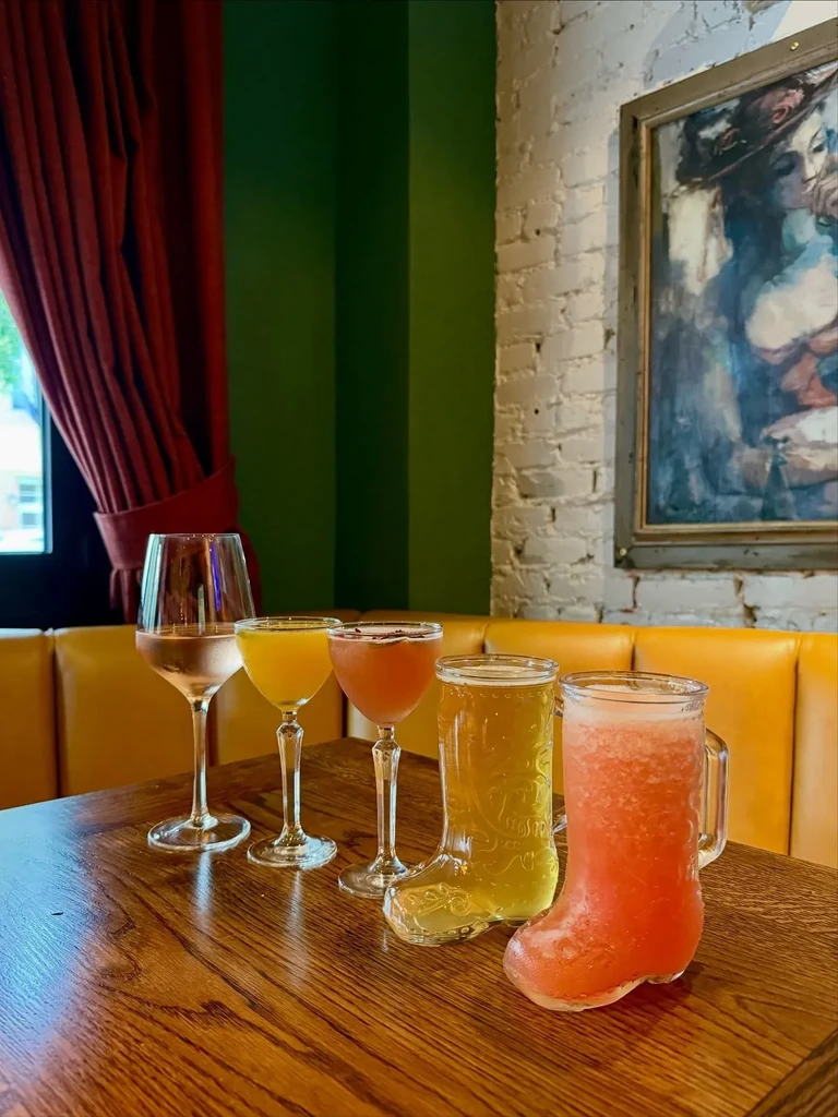 Five cocktails, two in boot-shaped glasses, on a wooden table.