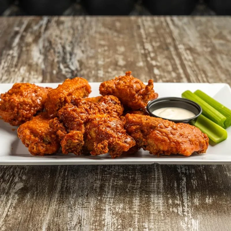 Crispy chicken wings with celery sticks and dip on a white plate.