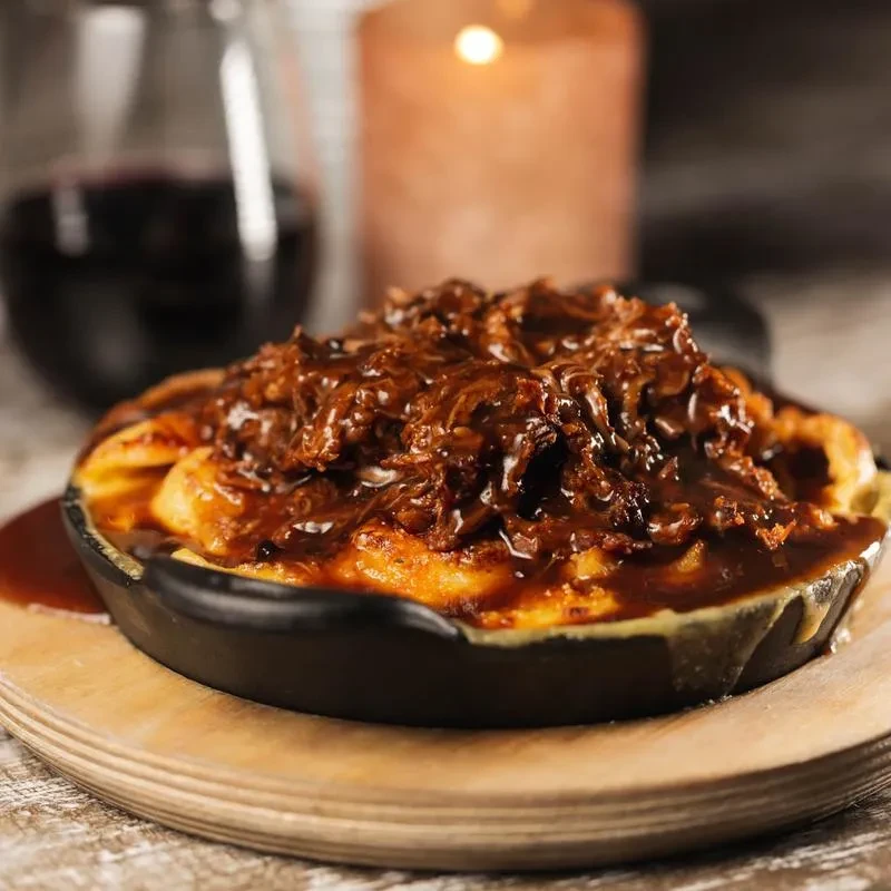 Pulled pork over mac and cheese in a skillet on a wooden board.
