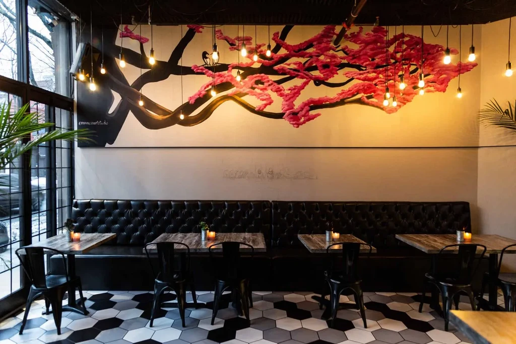 Restaurant interior with a black banquet, small tables, and a large tree mural.