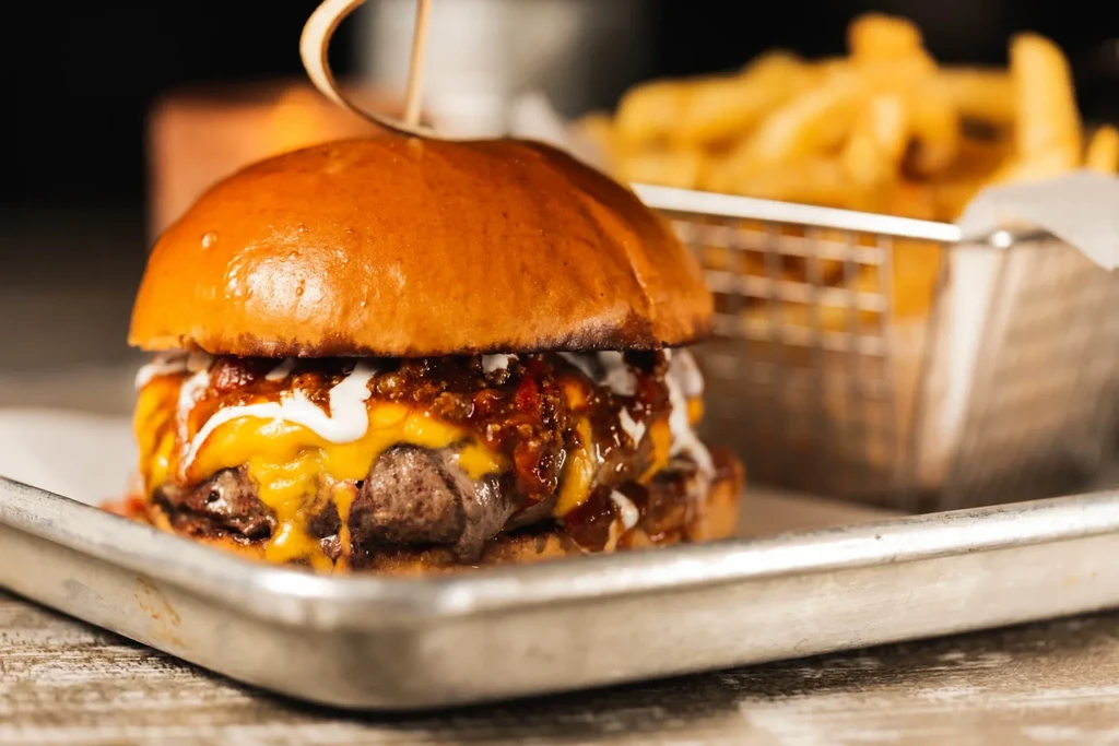 A loaded cheeseburger and fries on a metal tray.