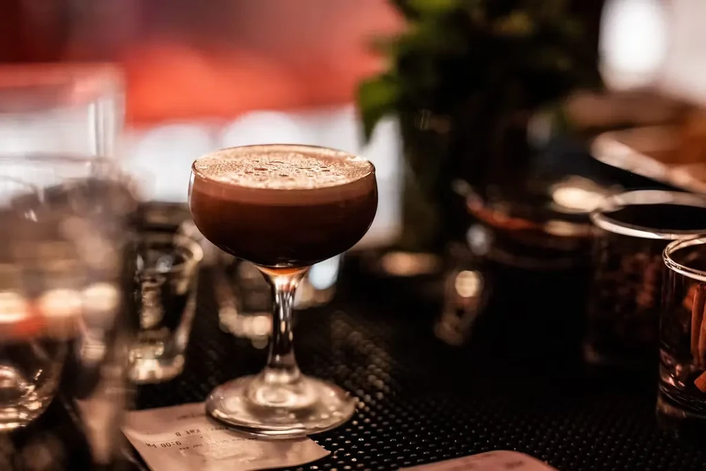 A dark cocktail with foam and sprinkled powder on a bar counter.