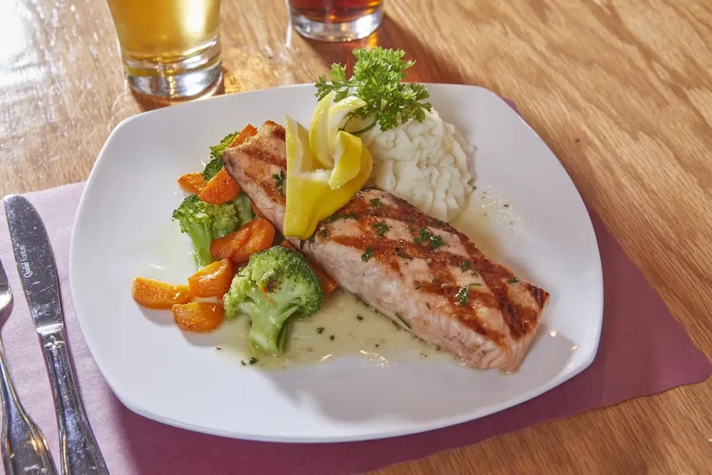 Grilled salmon, mashed potatoes, broccoli, and carrots on a white plate.
