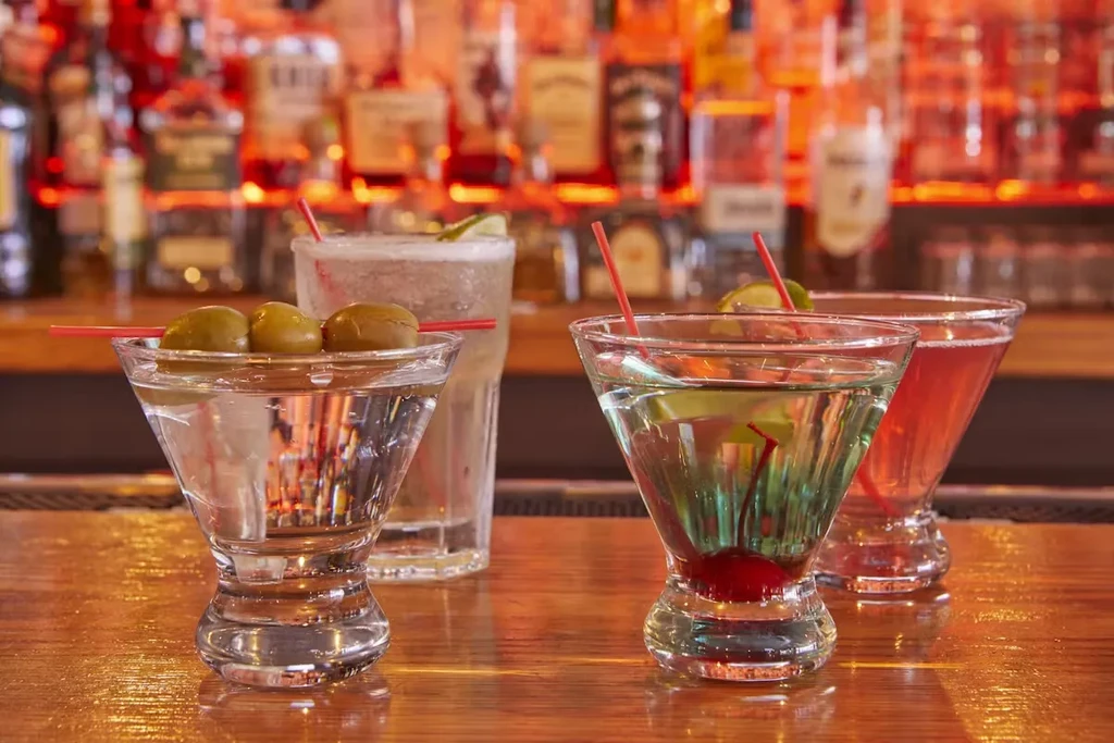 Three cocktails with straws and garnishes on a bar counter.