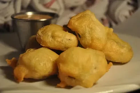 Golden fried hushpuppies served with a dipping sauce in a metal cup.