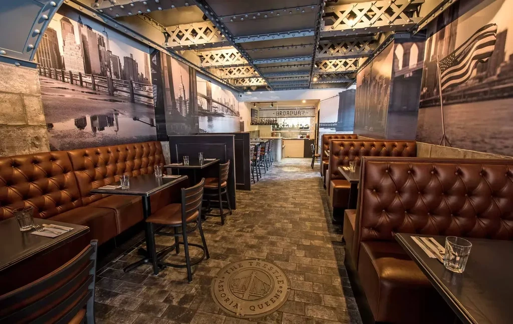 Restaurant interior with brown booths, brick walls, and NYC mural wallpaper.