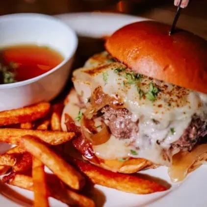 A French Dip burger with fries and a cup of au jus.