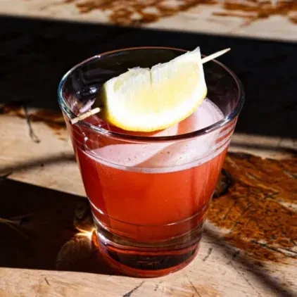 A red cocktail in a glass with a lemon wedge garnish.