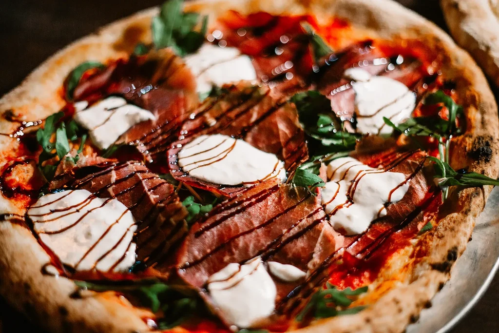 Pizza with prosciutto, mozzarella, arugula, and balsamic glaze.