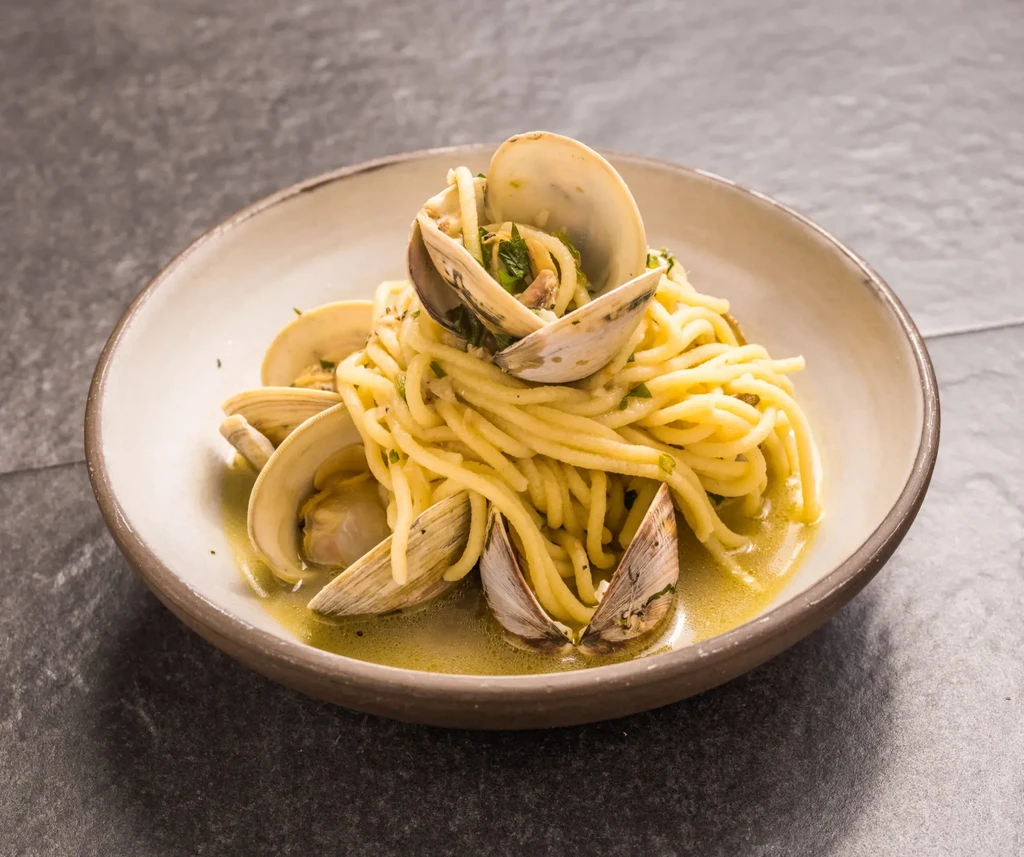 Spaghetti with clams in a light broth, served in a beige bowl.