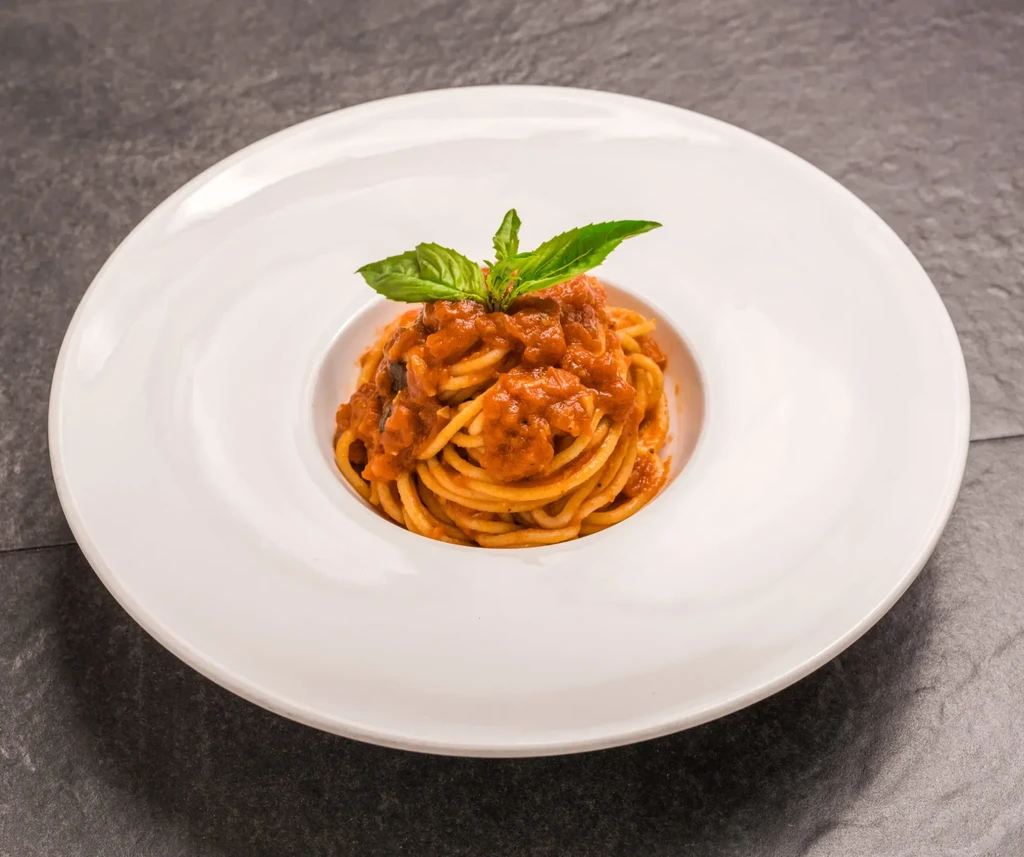 Spaghetti pasta with red sauce and a sprig of basil in a white bowl.