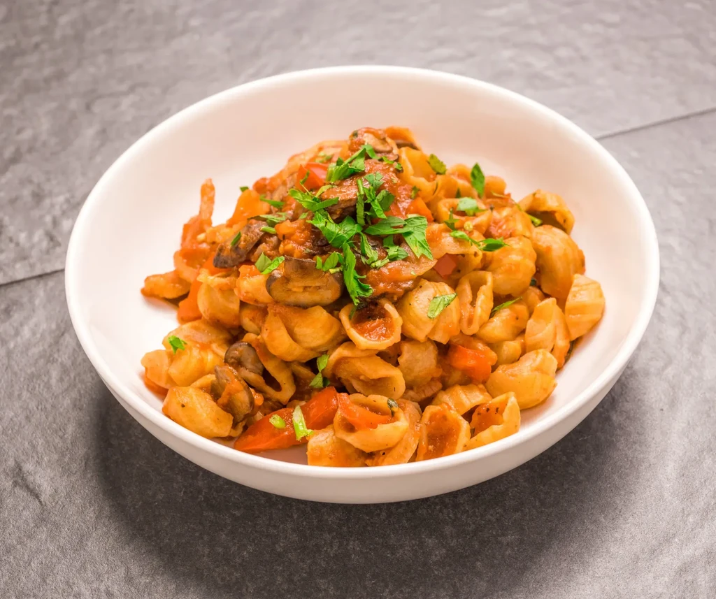 A bowl of orecchiette pasta with tomato sauce, mushrooms, and parsley.