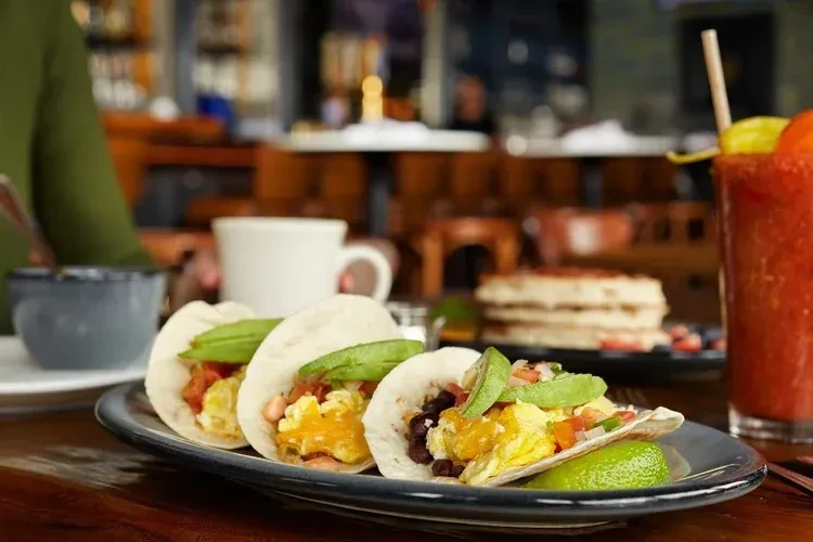 Close-up of breakfast tacos, pancakes, coffee, and a red drink.