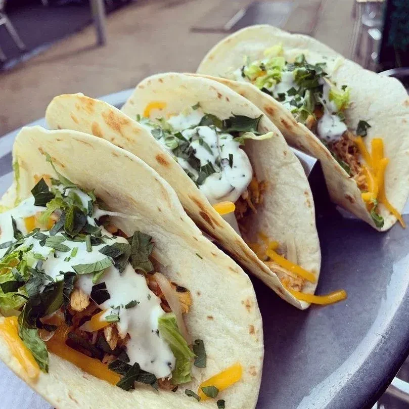 Four chicken tacos with cheese, lettuce, and sour cream on a tray.