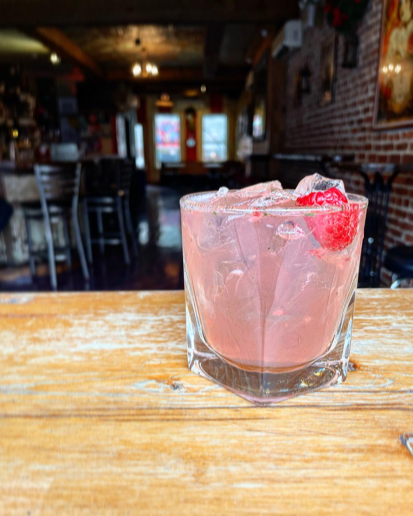 Pink iced drink with raspberries in a glass on a wooden table.