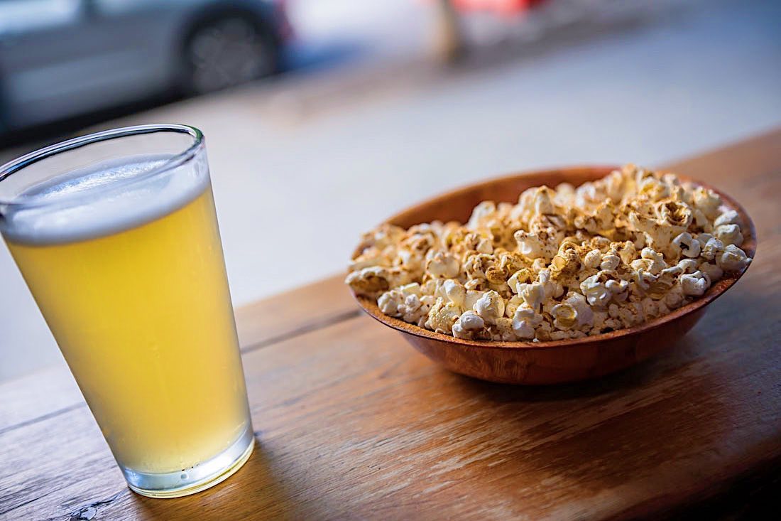 A glass of beer and a bowl of seasoned popcorn on a wooden table.