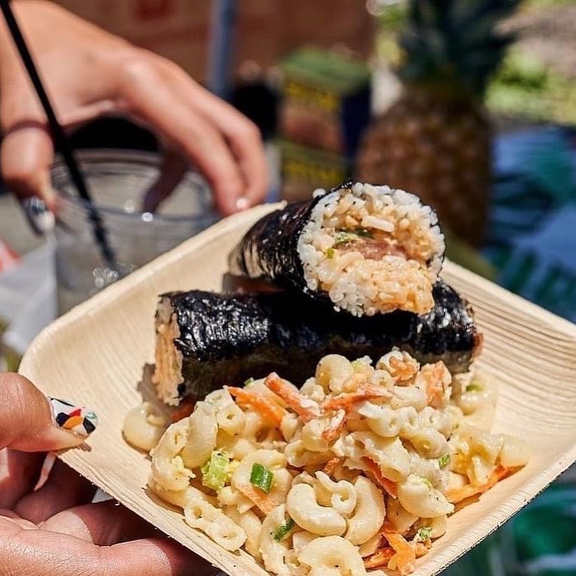 Hand holding plate with two large sushi rolls and macaroni salad.