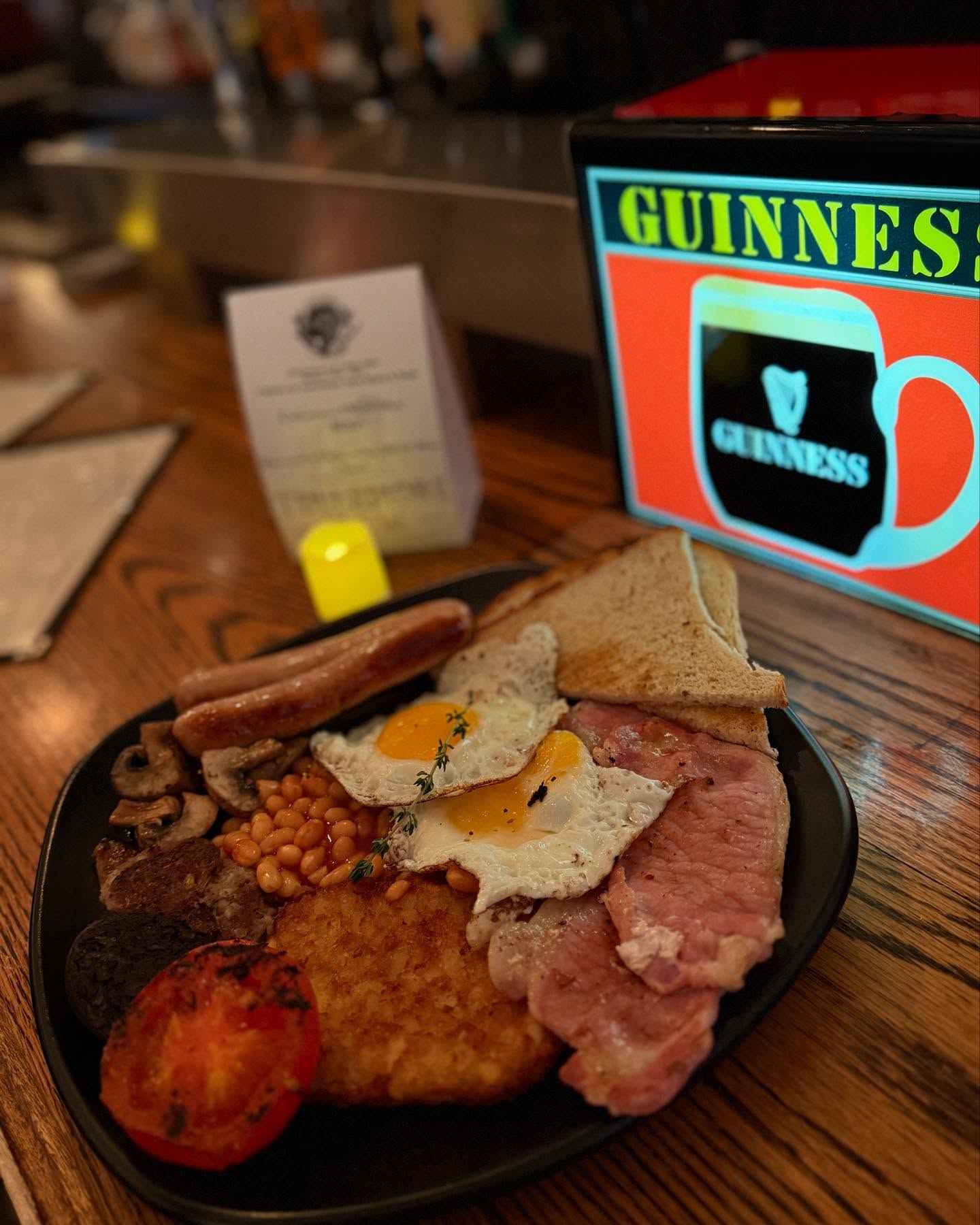 Full English breakfast on a plate with a glowing Guinness sign.