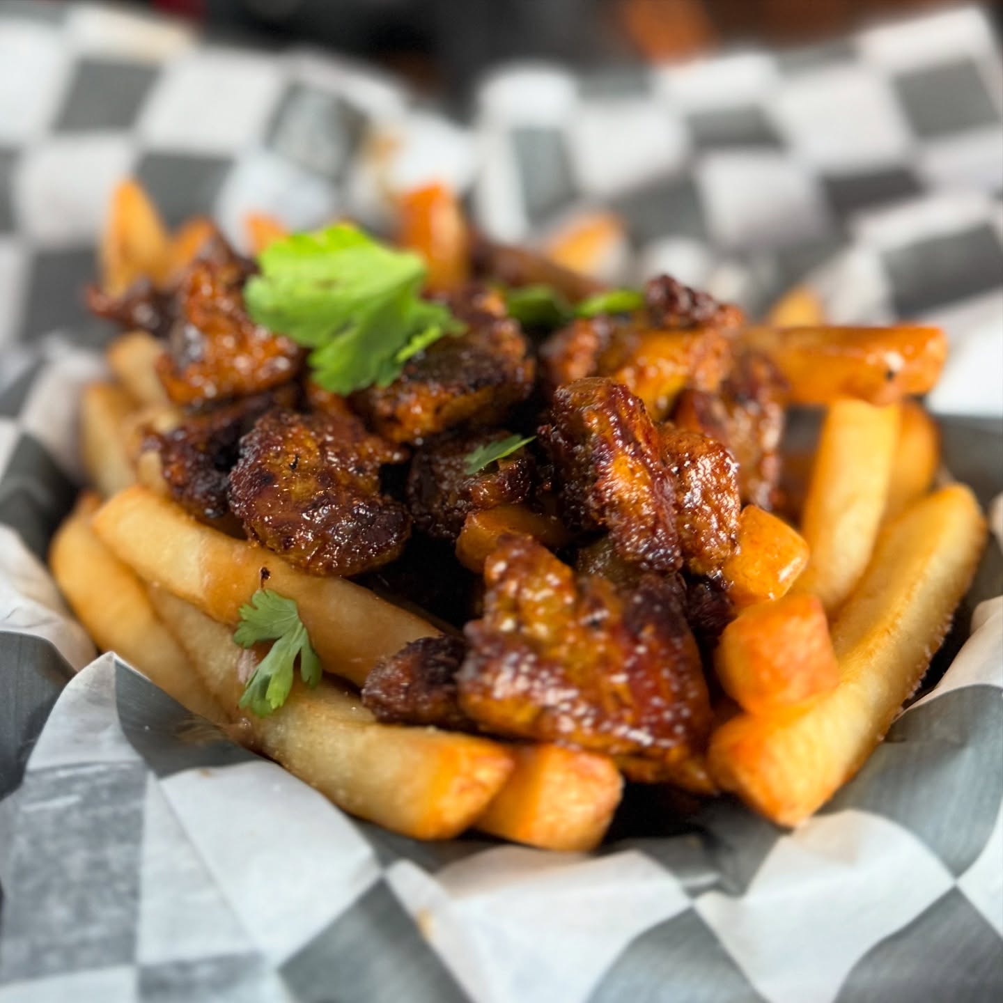 French fries and dark glazed meat with fresh green herbs in a basket.